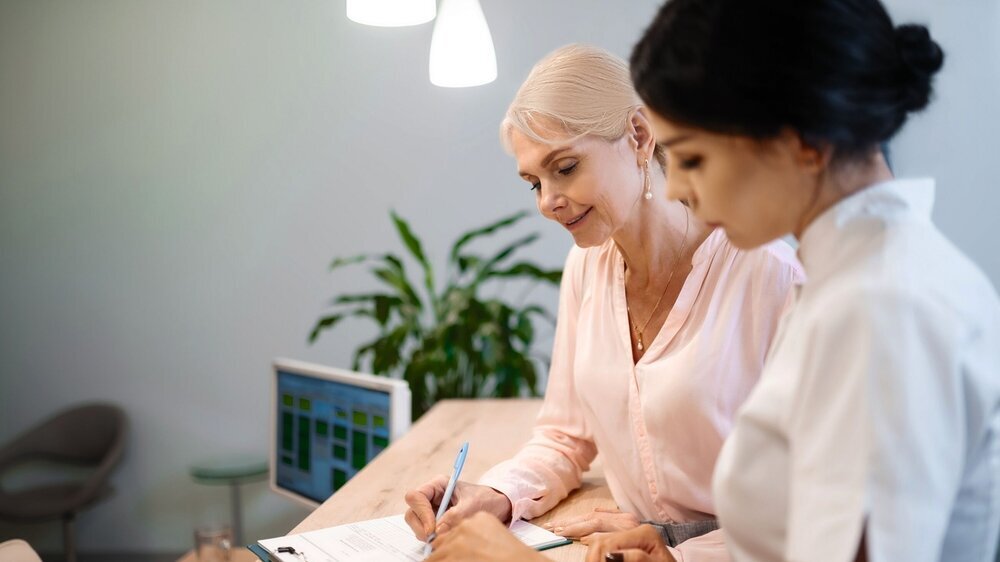 Woman signing a contract with her dentist. Making arrangements. Smiling woman standing near her attentive dentist and signing a contract with her.