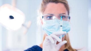 Dentist in mask and glove holding an injection