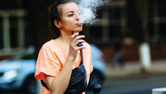 Pretty young hipster woman vape ecig, vaping device at the sunset. Toned image. Vaping