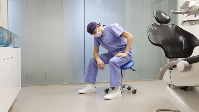 Tired dentist in his office sitting on stool, having break,waiting for patient in his office