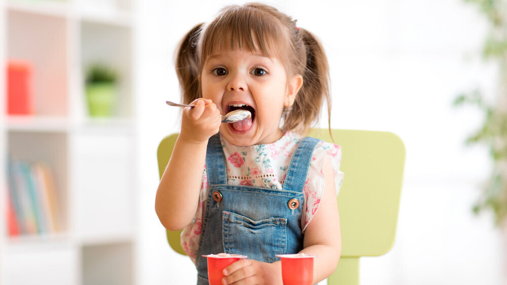 Cute little girl eating yogurt. Joghurt Kind