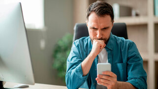 Gestresster Mann schaut skeptisch auf sein Smartphone.