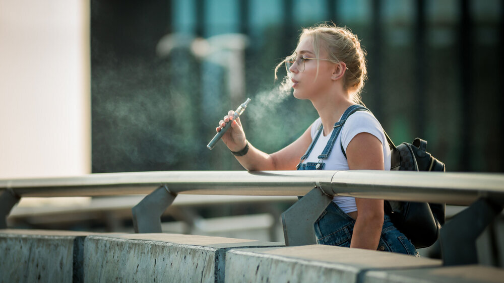 Junge Frau im Freien vaping E-Zigarette auf moderne Stadt Gebäude Hintergrund Junge Frau im Freien vaping E-Zigarette auf moderne Stadt Gebäude Hintergrund
