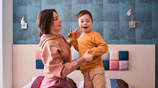 Junge mit Down-Syndrom spielt mit seiner Mutter auf dem Bett im Schlafzimmer