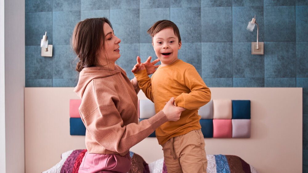 Junge mit Down-Syndrom spielt mit seiner Mutter auf dem Bett im Schlafzimmer