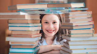 Kind sitzt zwischen Bücherstapeln und lacht