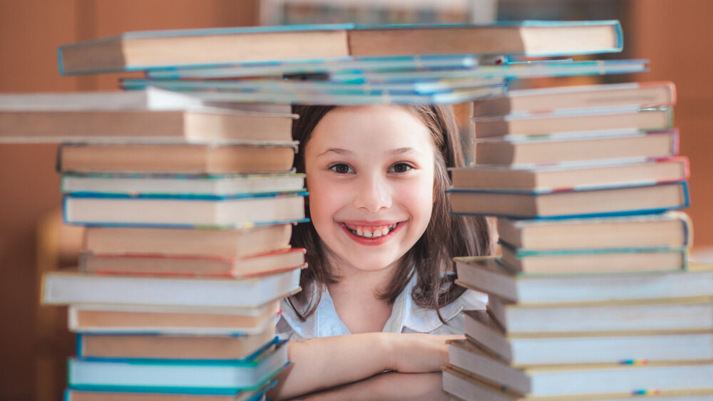 Kind sitzt zwischen Bücherstapeln und lacht