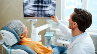 Back view of male dentist pointing at tooth X-ray image on screen during consultation in modern dental clinic