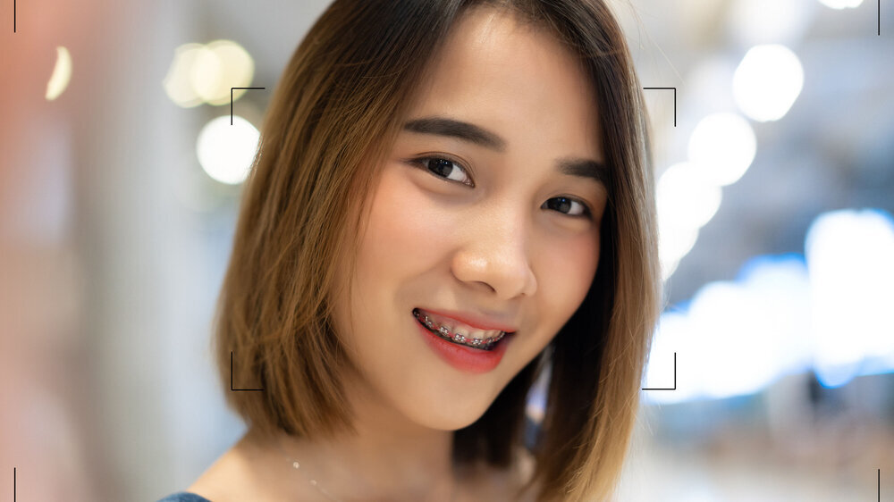 Closeup portrait of caucasian Asian lady wearing dress jeans smilling and make selfie recording video vlog from hands with mirrorless camera at airport. Concept Vlog live streaming. Zahnspange