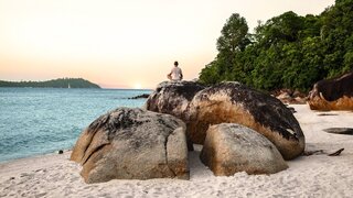 Young Man Meditating and doing Yoga Exercises against beautiful ocean view on stones.