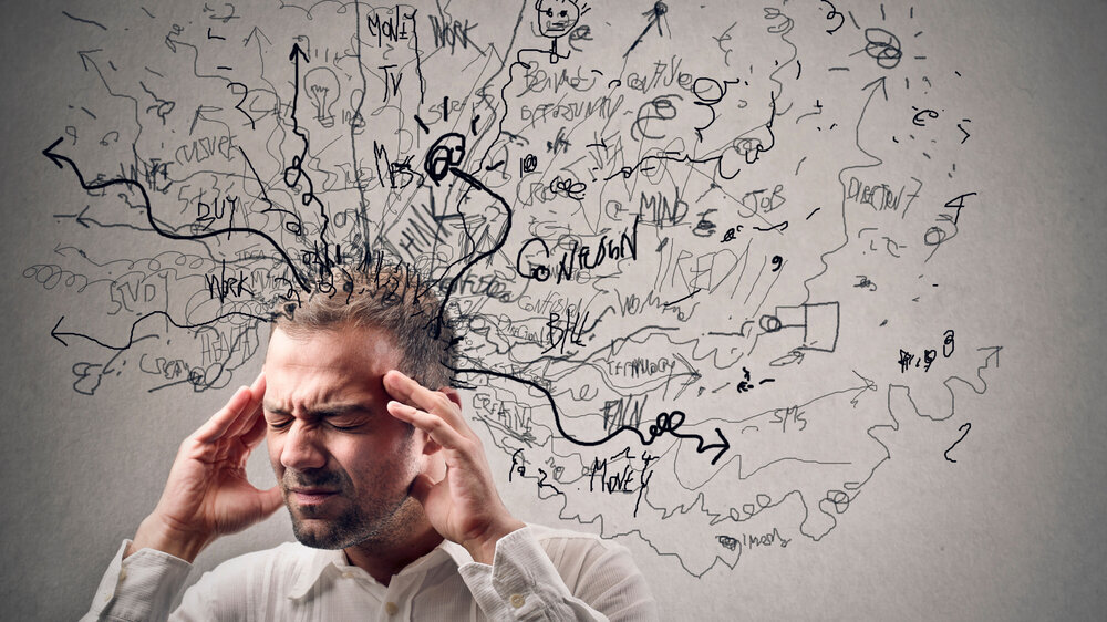 Ein gestresster Mann hält sich die Schläfen, über seinem Kopf schwirren stilisiert ungeordnete Gedanken