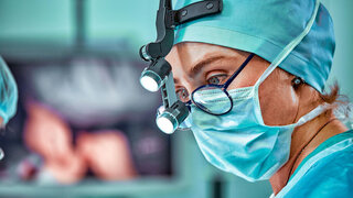 Chirurgin im Operationssaal mit Spiegelung in der Brille.