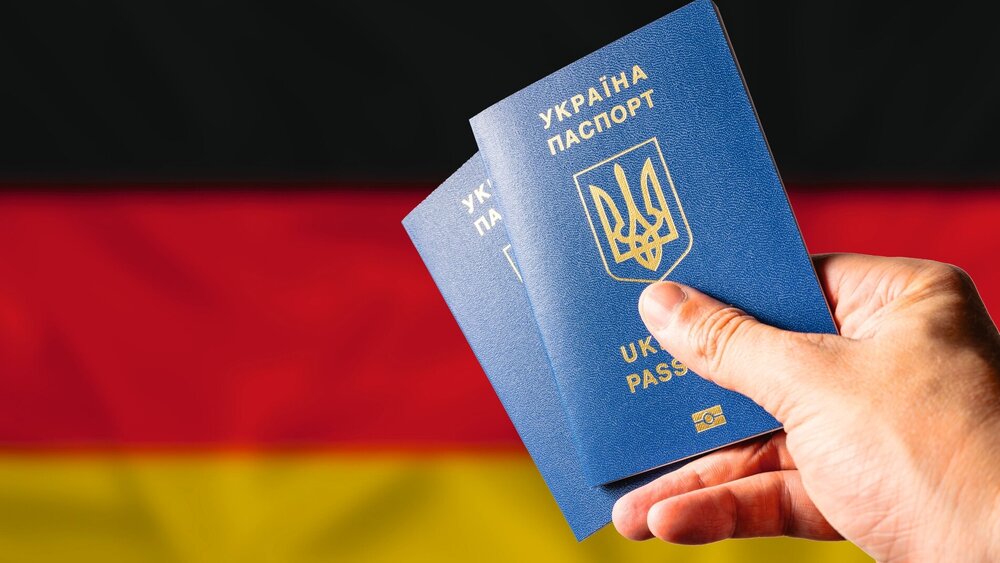 Two Ukrainian biometric passports in a woman's hand against the background of the national flag of Germany. Trips of Ukrainian citizens to Germany, Tourism, work, study, war in Ukraine.