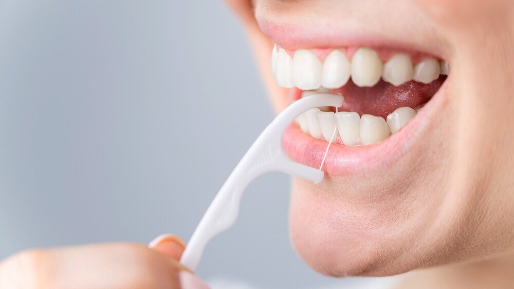 Caucasian woman brushing teeth with toothpick with dental floss on white background. Interdentalbürste