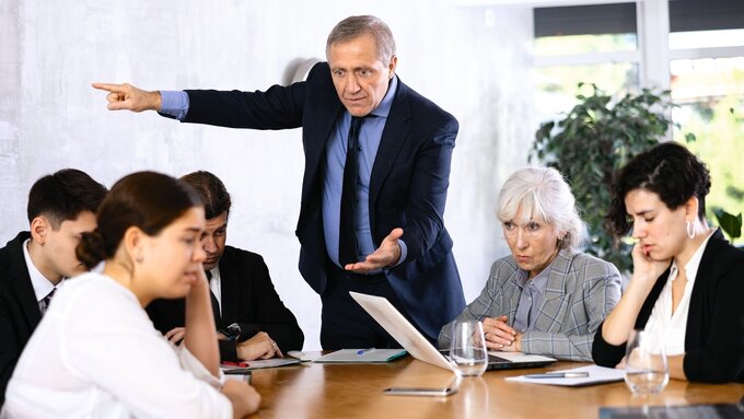 Wütender Chef zeigt auf Mitarbeiterin und schimpft.