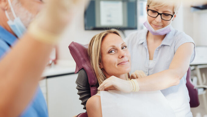 Woman smiling as the dental nurse attends to her at the start of a consultation in the surgery viewed past the dentist