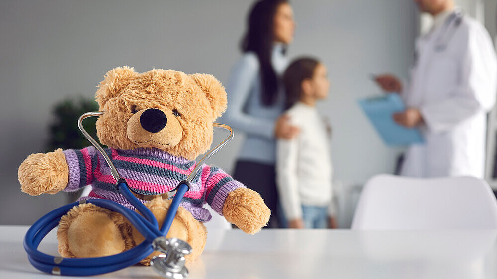 Cute soft teddy bear doctor with stethoscope sitting on table at pediatric clinic or children's medical center. Kids checkup visit to hospital, health maintenance concept. Blurred empty space for text