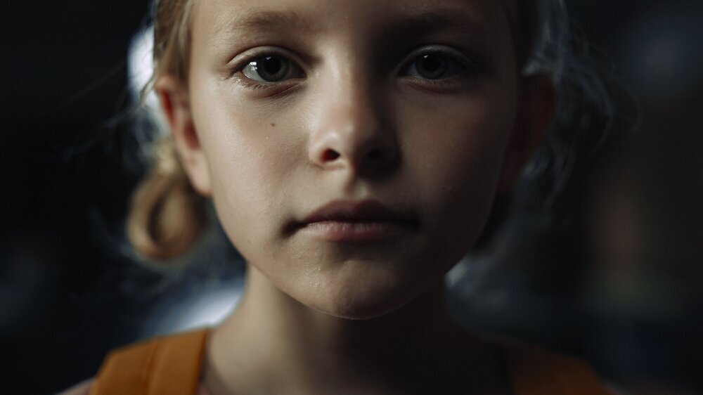 Closeup face frightened girl in dark hall. Schoolgirl standing school corridor. trauriges Kind