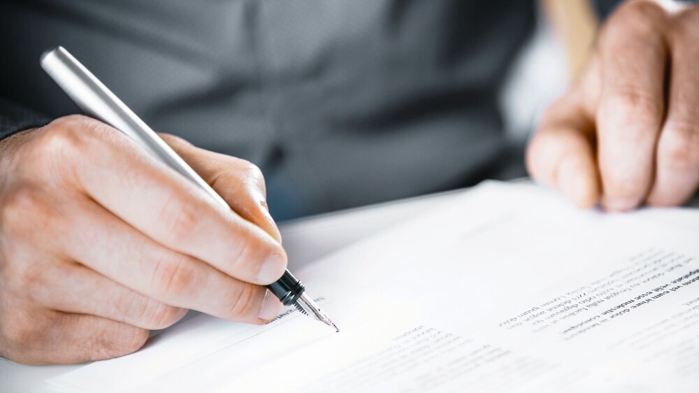 Man signing a contract or agreement Close up of the hand of a man signing a contract or agreement with a fountain pen at the end of a block of text