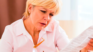 Senorin liest Beipackzettel eines Medikaments und schaut dabei fragend.