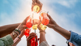 Group of friends toasting with colorful drinks - summer celebration, joyful moments, outdoor party vibe - happy young adults raising drinks in the sky.