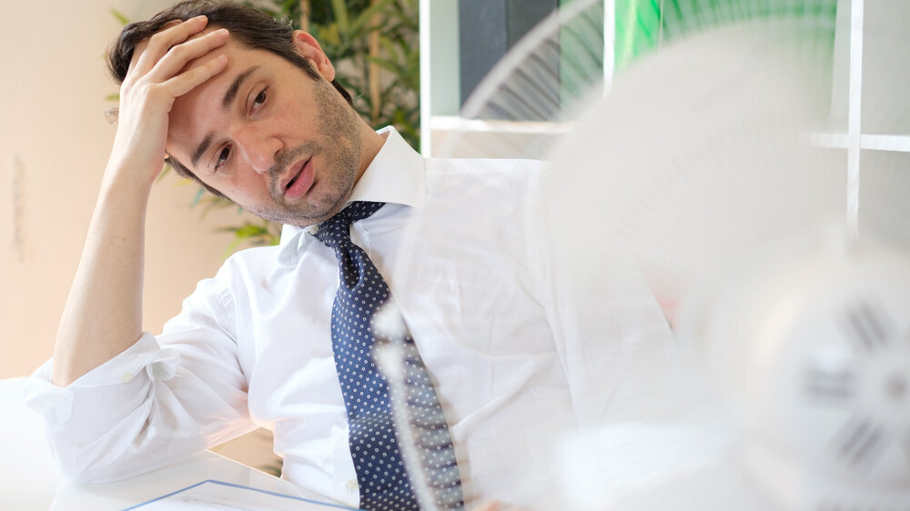 Office employee feeling stressed after summer heat haze Businessman trying to refresh at work in summer heat