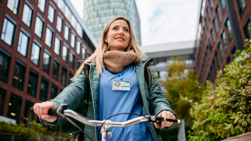 Beautiful nurse commuting through the city by bike. Doctor city leaving hospital by bike after long workday. Ärztin auf Fahrrad