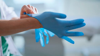 Arzt zieht sich Handschuhe an in Vorbereitung auf medizinischen Eingriff.