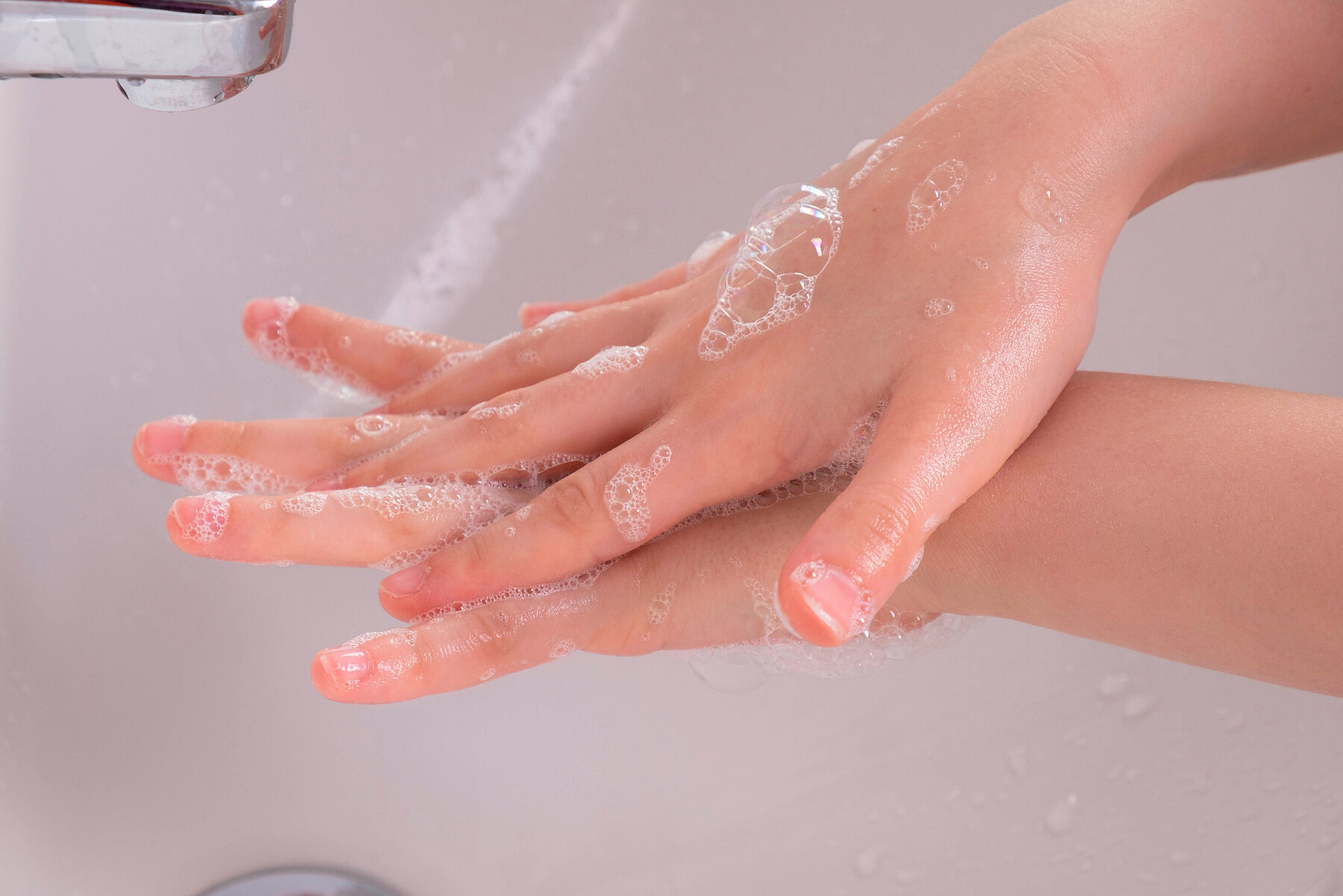young girl soaped her hands and holds them under the tap in the bathroom in the morning