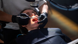 Restorative Dentist Operating On Patient Mouth Using Microscope And Rotary Instruments, Gloved Hands