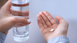 Hand mit Glas Wasser und Tablette