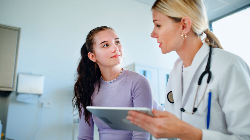 Young woman doctor explaining diagnosis to teenage girl in her ambulance. Young woman doctor explaining diagnosis to teenage girl in her ambulance office.