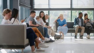 Verschiedene Menschen sitzen im Wartebereich einer Arztpraxis