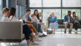 Verschiedene Menschen sitzen im Wartebereich einer Arztpraxis