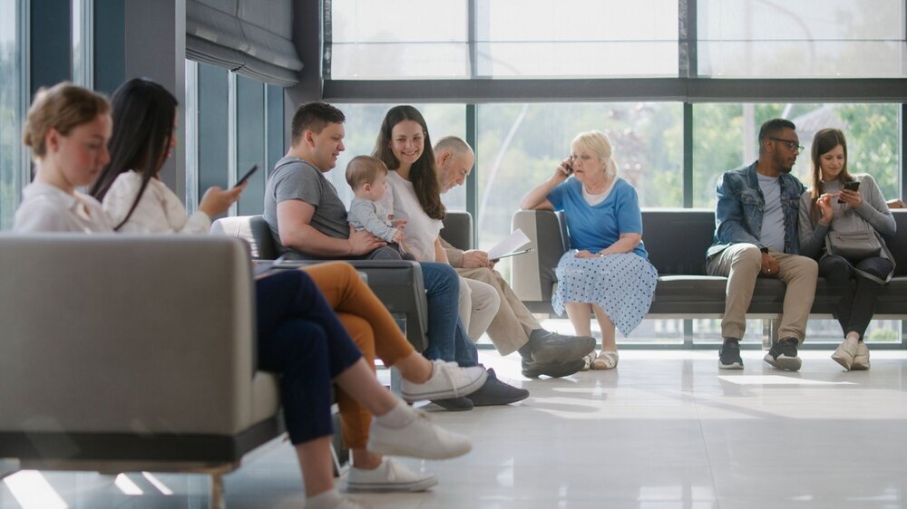 Verschiedene Menschen sitzen im Wartebereich einer Arztpraxis