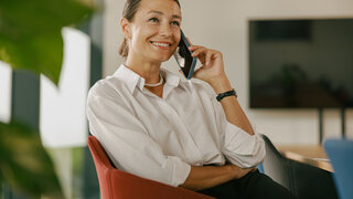 Eine selbstbewusste Frau, die lächelt und ein Telefongespräch in einem modernen Büro führt