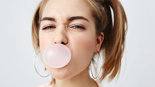 Stilvolles, charmantes, hübsches Mädchen im Teenageralter mit zwei Pferdeschwänzen, das die Augen verdreht und ein rosa Kaugummi im Mund hat