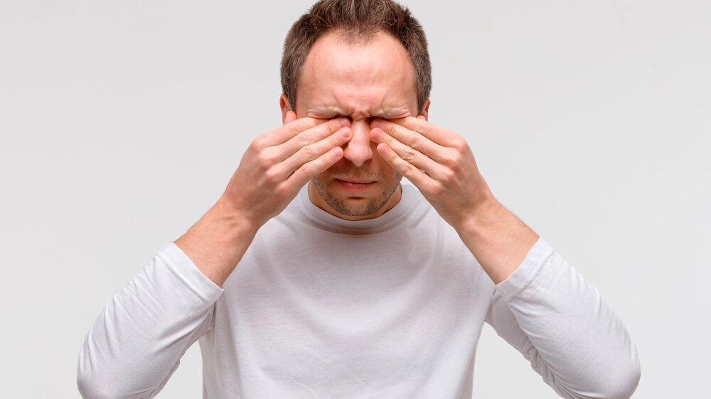 Close up of man has a problem with contact lenses, rubbing his swollen eyes due to pollen, dust allergy. Dry eye syndrome, watery, itching. Isolated on grey background, front view. Mann mit Augenproblemen