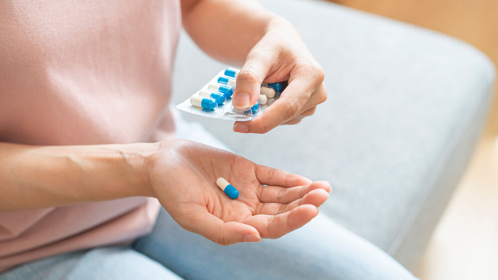 Frau entnimmt Antibiotikakapsel auf Bister und hält ihre Hand auf.