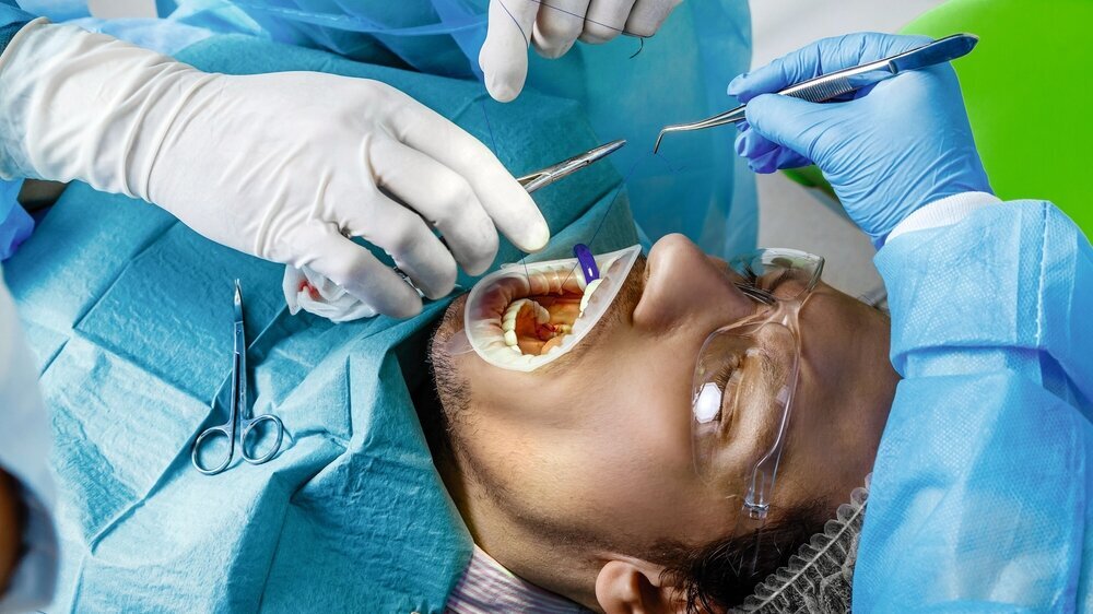 Close-up shot of attentive doctors performing surgical operation installing dental implants into patient's mouth in modern dental clinic. Dental instruments. Stomatology clinic. Dental surgery. Close-up shot of attentive doctors performing surgical operation installing dental implants into patient's mouth in modern dental clinic. Dental instruments. Stomatology clinic. Dental surgery.