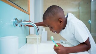 Junge putzt Zähne am Waschbecken und betätigt Wasserhahn