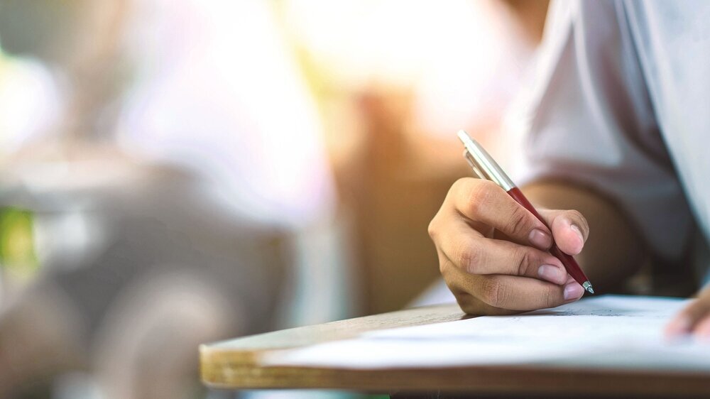 Closeup to hand of student holding pen and taking exam in classroom with stress for education test . Closeup to hand of student holding pen and taking exam in classroom with stress for education test .