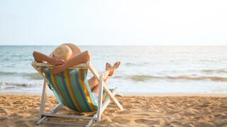 Sommerurlaub am Strand, Frau mit Hut entspannt sich auf einem Liegestuhl am Strand.