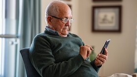 Old man wearing eyeglasses to use smartphone at home. Handsome senior man at home relaxing on couch reading a message on cellphone. Senior sitting alone in his living room and using mobile phone.