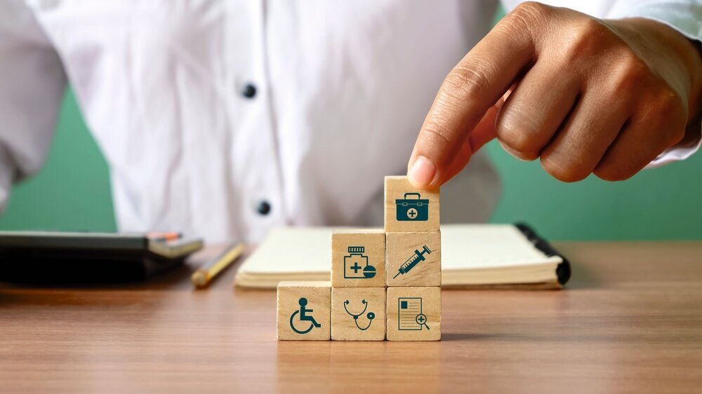 Close-up of human hand stacking wooden blocks overlapping health care icons and medical icons. The concept of choosing health insurance rights when sick Close-up of human hand stacking wooden blocks overlapping health care icons and medical icons. The concept of choosing health insurance rights when sick
