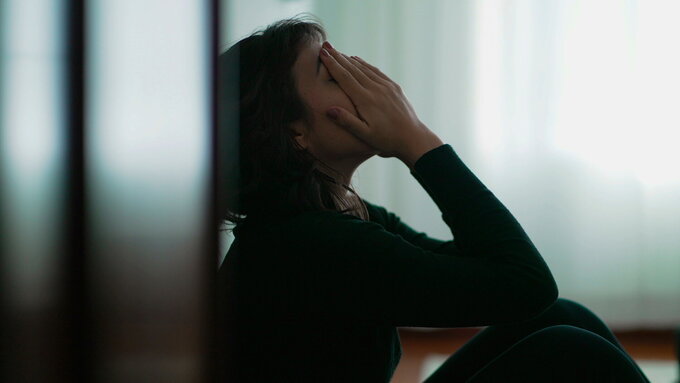 Depressive Frau sitzt auf dem Fußboden und vergräbt verzweifelt das Gesicht in den Händen.
