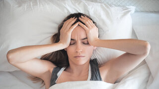 Frau mit Kopfschmerzen im Bett, gestresst