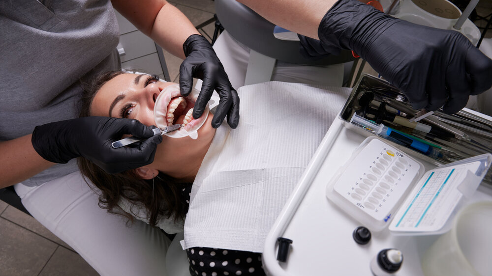Junge Frau liegt auf einem Zahnarztstuhl und erhält Brackets für eine Zahnspange Junge Frau liegt auf einem Zahnarztstuhl und erhält Brackets für eine Zahnspange