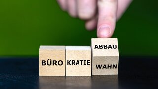 Hand dreht Würfel und ändert den Ausdruck Bürokratiewahn in Bürokratieabbau.
