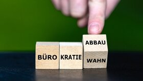 Hand dreht Würfel und ändert den Ausdruck Bürokratiewahn in Bürokratieabbau.